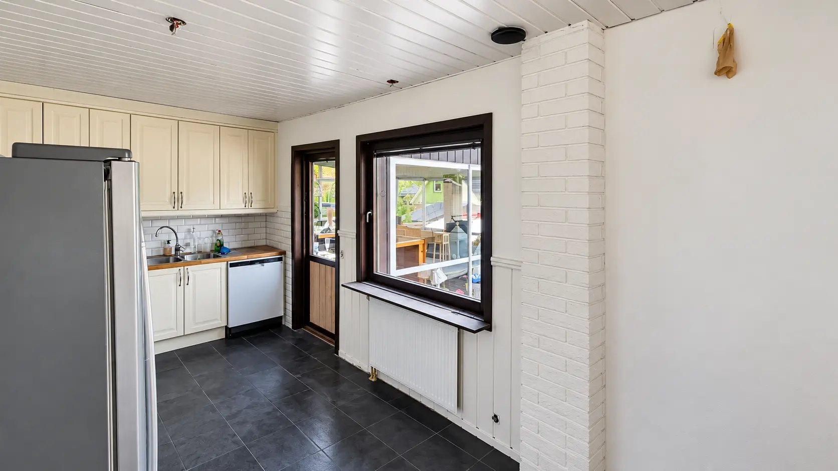 Vitmålat kök med tegelpelare, skåp och mörk bänkskiva.